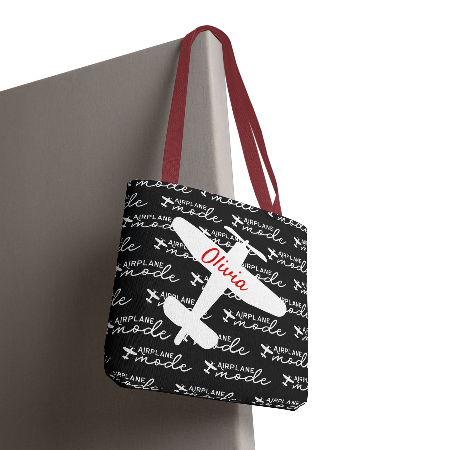 Black tote bag with airplane mode text and red handles on a gray surface