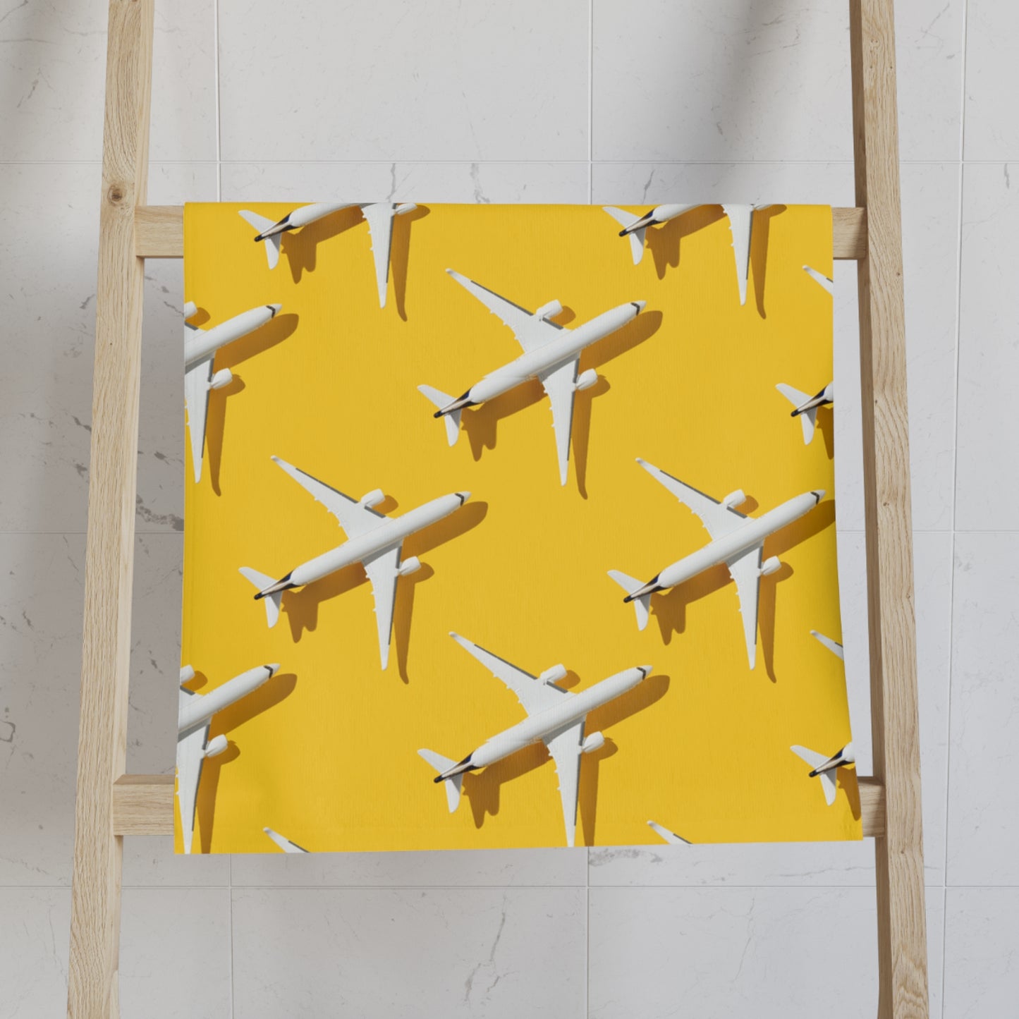 Yellow tea towel with jet plane pattern by AviatrixA draped on a wooden ladder against a tiled wall.