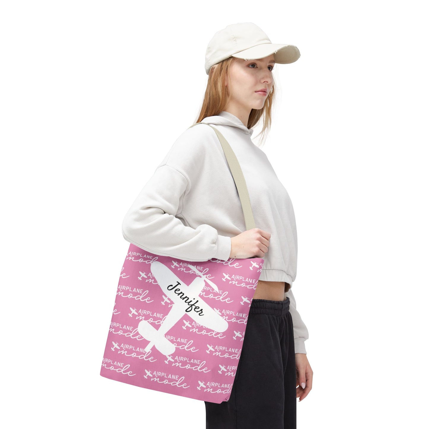Person holding a pink tote bag with text and a name on it, wearing a white cap and white sweatshirt.