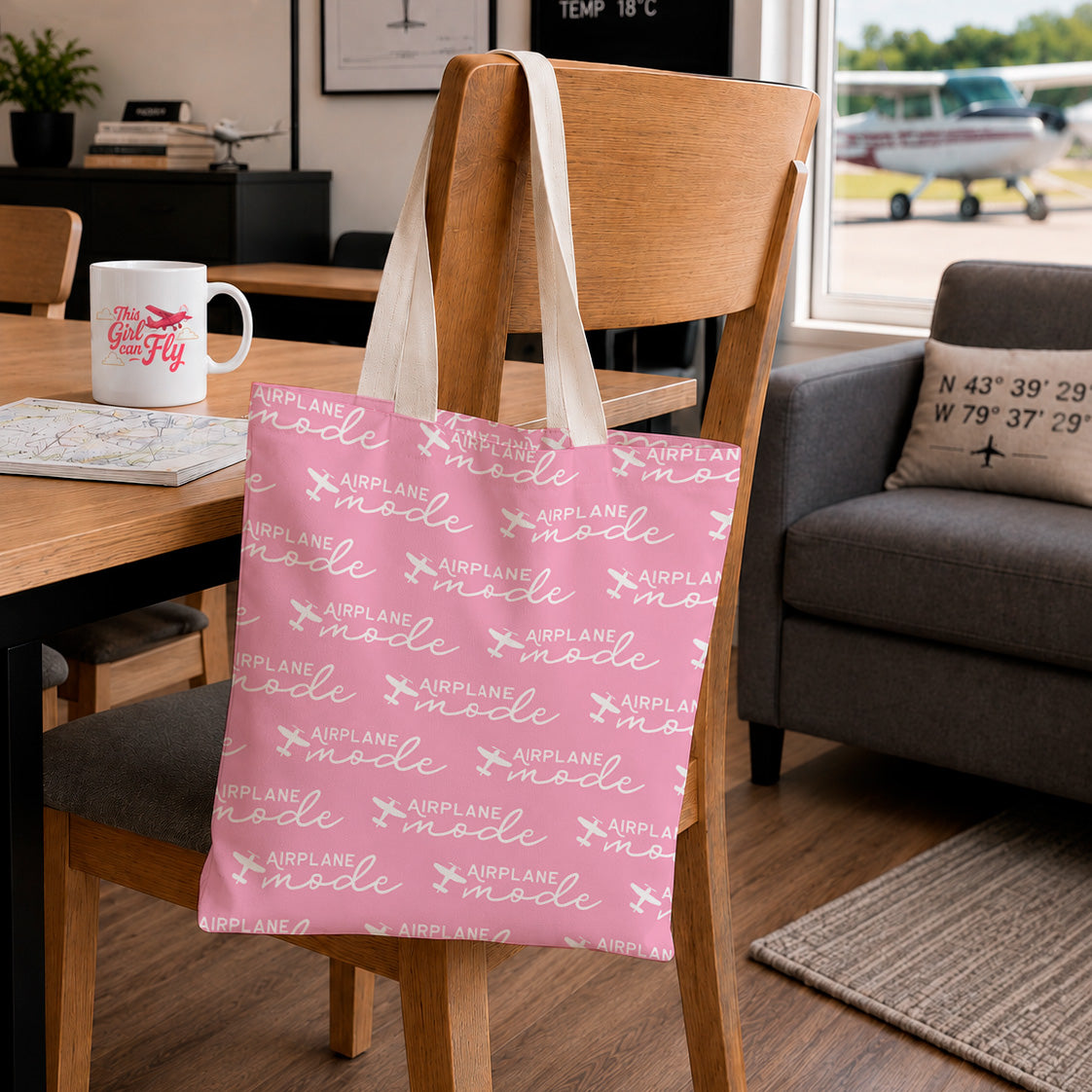 A pink fabric tote bag with a white 'AIRPLANE mode' pattern hangs from the back of a wooden chair in a cozy living room setting.