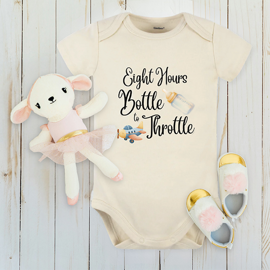 Baby onesie with 'Eight Hours Bottle to Throttle' text, plush lamb toy, and baby shoes on a wooden surface