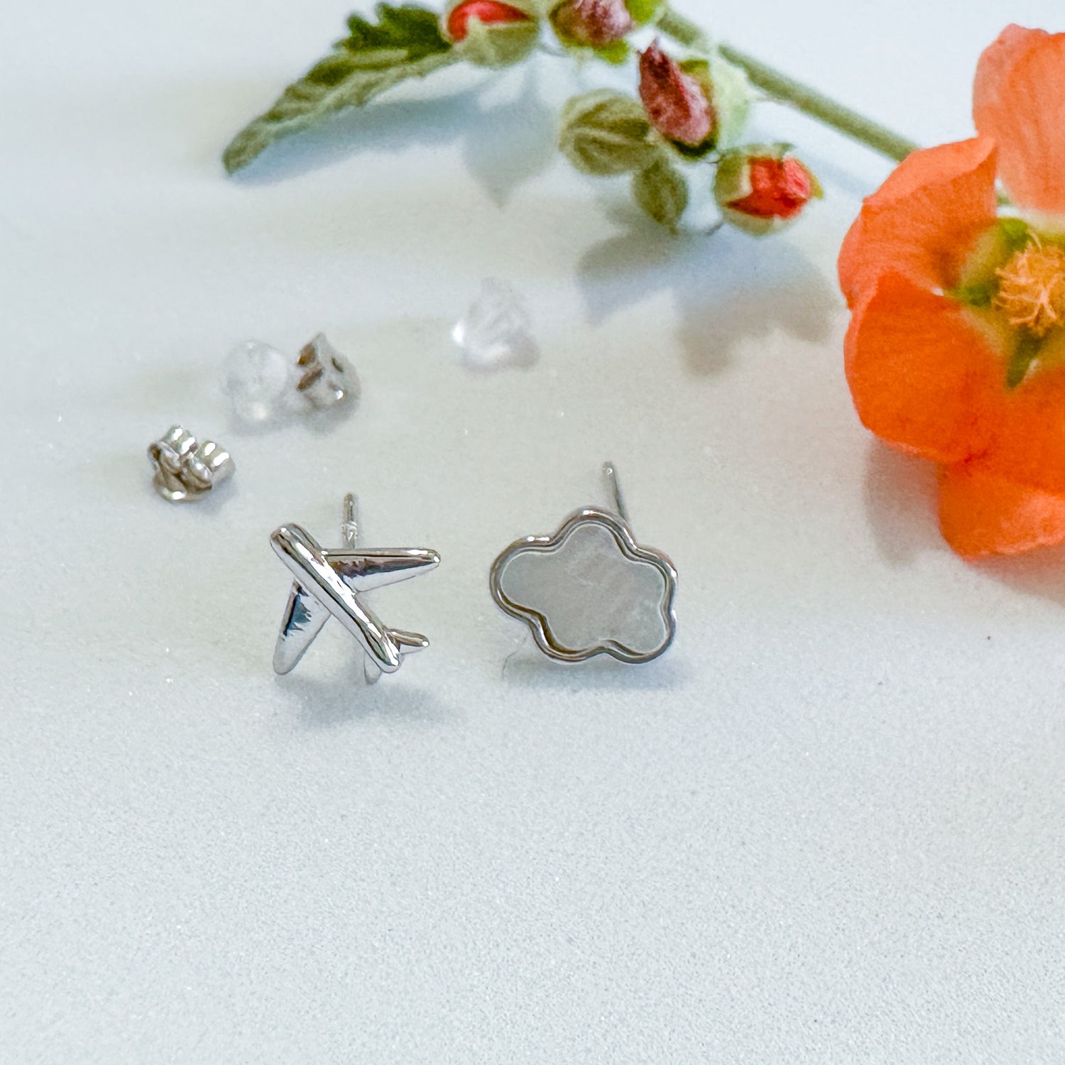 Asymmetric stud earrings of cloud and plane by AviatrixA with silver hardware and floral decorations.