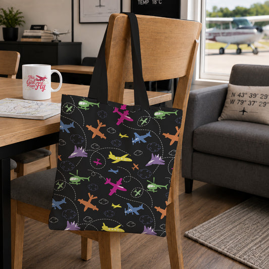 A black tote bag with a colorful airplane pattern hangs on a wooden chair in a modern living room setting.