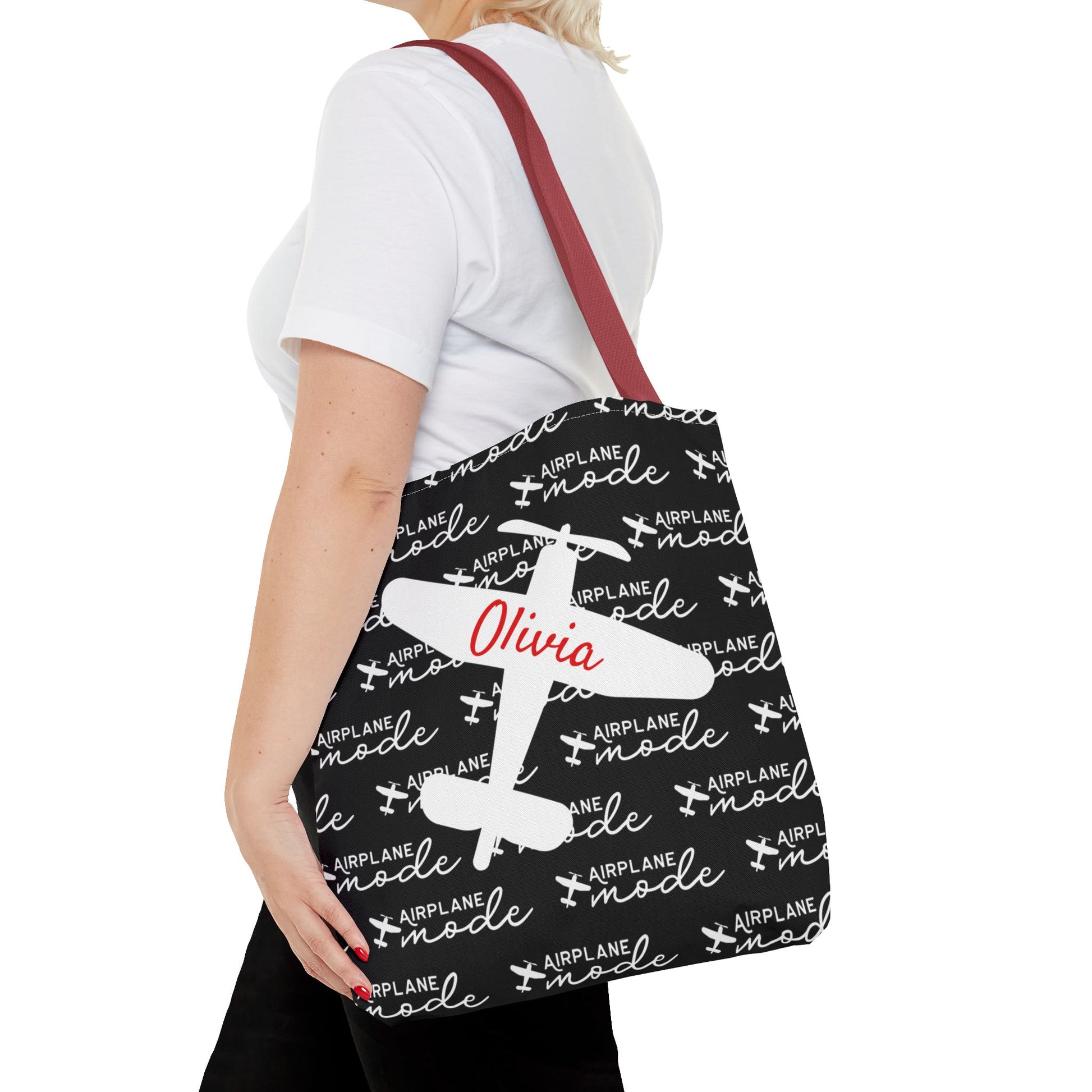 Person holding a tote bag with airplane mode pattern and name 'Olivia'.
