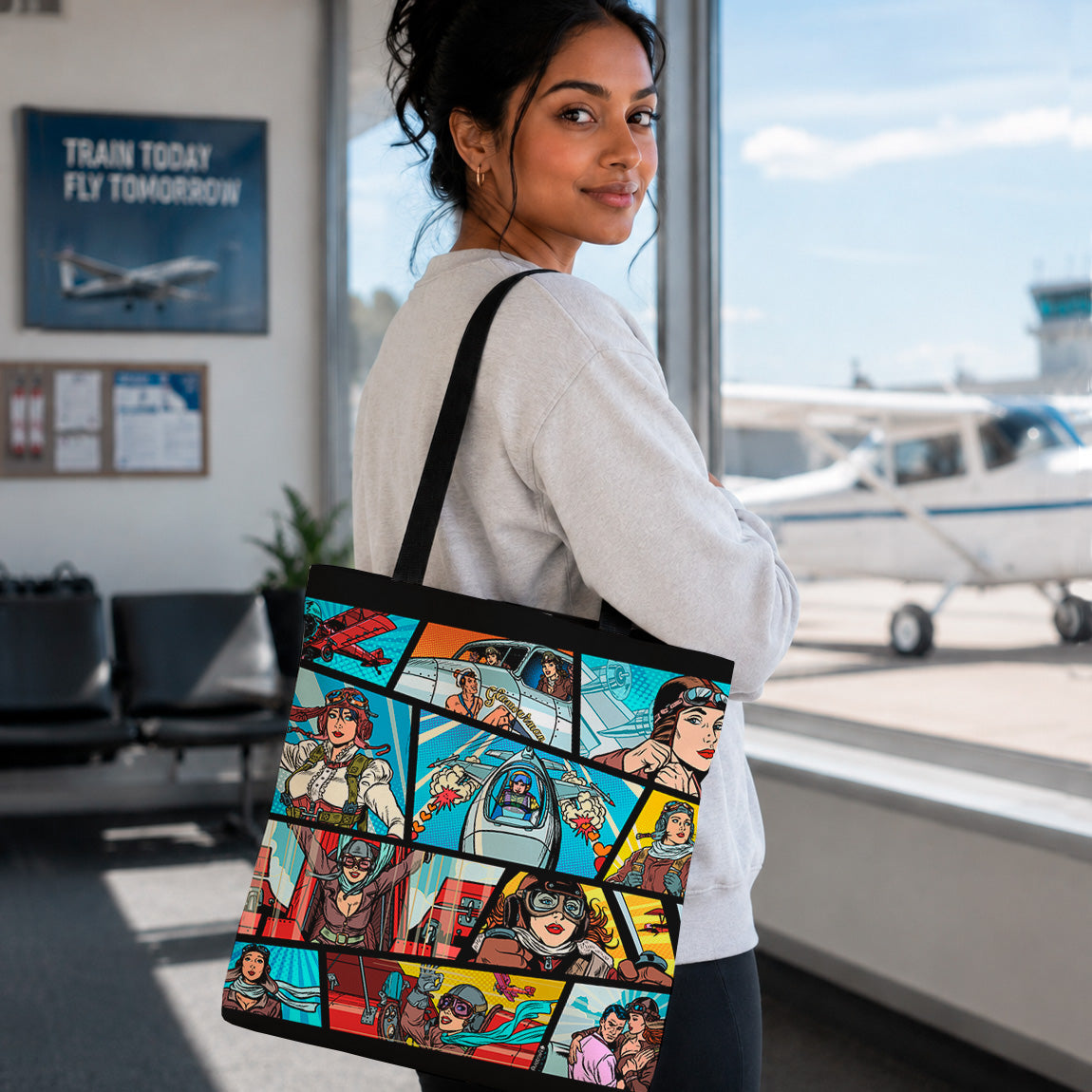 A woman standing in an airport terminal holding a black tote bag printed with a colorful comic-style collage of characters and scenes. A small airplane is visible through the window behind her.