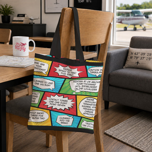 A canvas tote bag with a colorful comic book panel print and black handles, hanging on a wooden chair in a living room setting.
